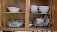 View of cabinet with stacked plain white plates and bowls, some patterned plates visible