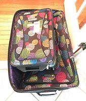 Two matching Tracker fabric suitcases with colorful polka dot pattern, nested with smaller placed inside larger, showing top and front pockets