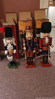 Three wooden nutcrackers standing in front of original boxes, showing full front view and relative size