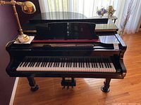 Front-right angle view of black baby grand piano showing lid partially open, bench, keyboard and three caster legs