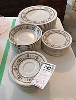 Stacked group of white porcelain dishes, bowls, and saucers showing patterned rims in brown, orange, and gold floral design.