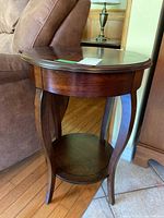 Side view of wooden round side table showing curved legs and lower shelf