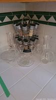 Chrome rotating spice rack with 12 glass spice containers, clear floral glass compote, glass plate, and glass dish on kitchen counter.