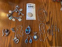 Sterling silver jewelry assortment with charm bracelet, pendants, chains, pins, and earrings displayed on wood surface