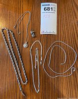 Overview photo of three chains, pendant, and earring set on wooden surface with lot tag.