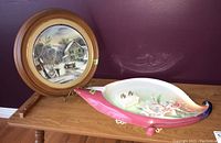 Photo showing the Franz decorative floral tray, Currier and Ives collector plate in frame, and multi outlet plug arranged on wooden table against purple wall.