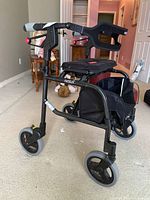 Front side view of the folding Nexus 3 Standard walker showing black frame, three wheels, padded seat, hand brakes, and storage bag.