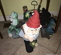 Photo showing plaster garden gnome with red hat holding shovel, two resin frogs sitting on rocks, metal tool caddy and garden figures.
