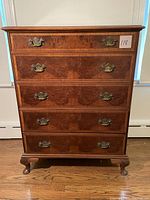 Front view of tall antique 5-drawer dresser showing brass handles and burl wood veneer drawer fronts.