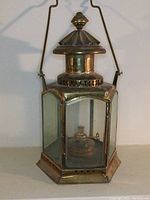 Full front view of hexagonal brass oil lamp lantern with handle and finial top.
