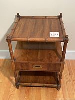 Full front view of the wooden Henredon end table showing bamboo style posts, top shelf, middle shelf and single drawer at bottom.