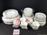Full set of dinnerware including stacked dinner plates, salad plates, soup bowls, fruit bowls, saucers, and teacups with some still wrapped in plastic.