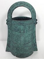 Front view of the patinaed metal vase showing textured geometric and figurative patterns with an arched handle