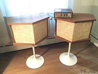 Two speakers on white metal pedestal stands with a wood-cased equalizer placed atop one speaker.