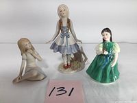 Three vintage decorative porcelain figurines together on a white surface, showing their full forms and scale.