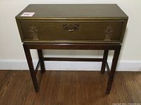 Front view of vintage entry table showing front panel with handle and decorative corner embellishments.