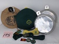 Two vintage canteens with canvas covers, a belt, scarves, and small patches and badges laid out on table.