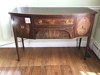 Front view showing curved bow-front design, central drawer and two round inlaid door panels