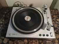 Philips 212 turntable on a marble surface, showing silver metal body, black platter and tonearm, model labeling and control buttons.
