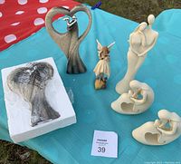 Photo showing all figurines on table with two stone Bride and Groom figurines, two white ceramic Mother and Child figurines, one ceramic Garden Fairy, and packaging for one stone figurine.