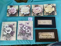 Overview photo showing the 4 canvas rose prints, 2 canvas pansy prints, and 2 wooden plaques arranged on a teal fabric.