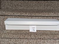 Single closed white bouquet box shown on carpeted stairs, with auction lot number card in front