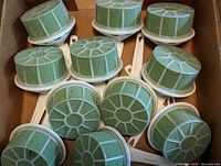 Eleven Lomey bouquet holders arranged in a box showing their green floral foam tops and white plastic bases and handles.