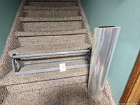 Wall mounted cello cutter positioned on stair steps alongside a tall, clear roll of crystalphane wrap.