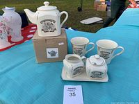 The full coffee and tea set including all seven pieces placed on a blue tablecloth outdoors with visible box for one teapot.