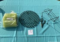 Photo showing all four items: pack of 100 yellow Gerbera sleeves, round floral grid rack, headstone saddle, and Gerbera rack on a blue surface.