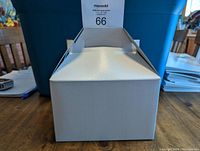 White takeout style box with handle, shown assembled and standing on table.