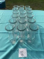 Eighteen clear glass Sabrina medium bud vases arranged in rows on a teal tablecloth outdoors.