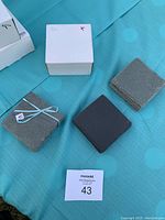 Four stacks of slate coasters, including a tied bundle, three colors visible, and white boxes in background.