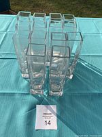 Overhead view of 14 clear square glass bud vases arranged in a cluster on a blue tablecloth outdoors.