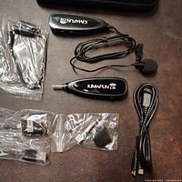 Complete wireless wearable lapel microphone kit laid out on table showing microphone, receiver, assorted cables, and adapters including iPhone and USB-C connectors.