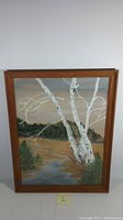 Framed watercolor painting showing entire artwork with a landscape and flowing stream with birch trees.