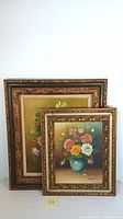 Two framed floral oil paintings of bouquets in vases positioned with smaller painting in front of larger one.