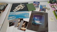 Full view of the lot showing NASA astronaut poster, art print, books, greeting cards, and signed dollar bill.