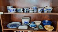 Display of Salmon Falls pottery including various bowls, a plate, condiment dishes, and a wall pocket on wooden shelf