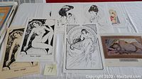 Photo showing seven fantasy art prints including signed and numbered lithographs by Steve Woron, Maria Cervantes, and Betty Page arranged on a white surface. Prints feature nude and semi-nude female fantasy figures in black and white and color.