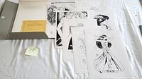 Photo showing the unopened hardcover portfolio case, multiple black and white art prints laid out in front, and a card with lot number.