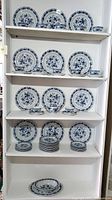 Shelves filled with stacked dinner plates, side plates, vegetable bowls, and teacups with saucers in blue floral pattern.