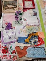 Top view of assorted handkerchiefs, napkins, and doilies showing various floral patterns and embroidery