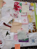 Top-down view of assorted vintage handkerchiefs, napkins, and doilies laid out on a table, showing varied floral patterns and embroidery.