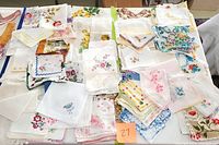 Wide view of various folded handkerchiefs and linens laid out, showing different sizes, embroidery and floral prints.