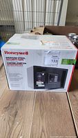 Photo of unopened Honeywell medium steel security safe box, showing brand, product name, and a picture of the safe with digital lock on front.