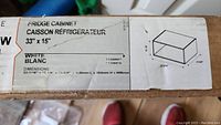 Close-up of the cabinet box label showing dimensions and color (white), and cabinet type for over fridge use.