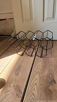 Photo of a black metal wine bottle holder rack showing hexagonal compartments for holding bottles horizontally on wood floor.