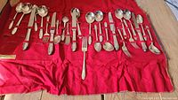 Photo of arranged silver plated cutlery on red cloth showing entire set size and variety