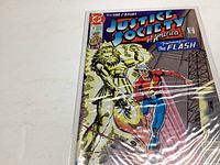 Photo of Justice Society of America comic book issue #1, featuring The Flash and a gold lion-like figure on the cover, in protective sleeve.